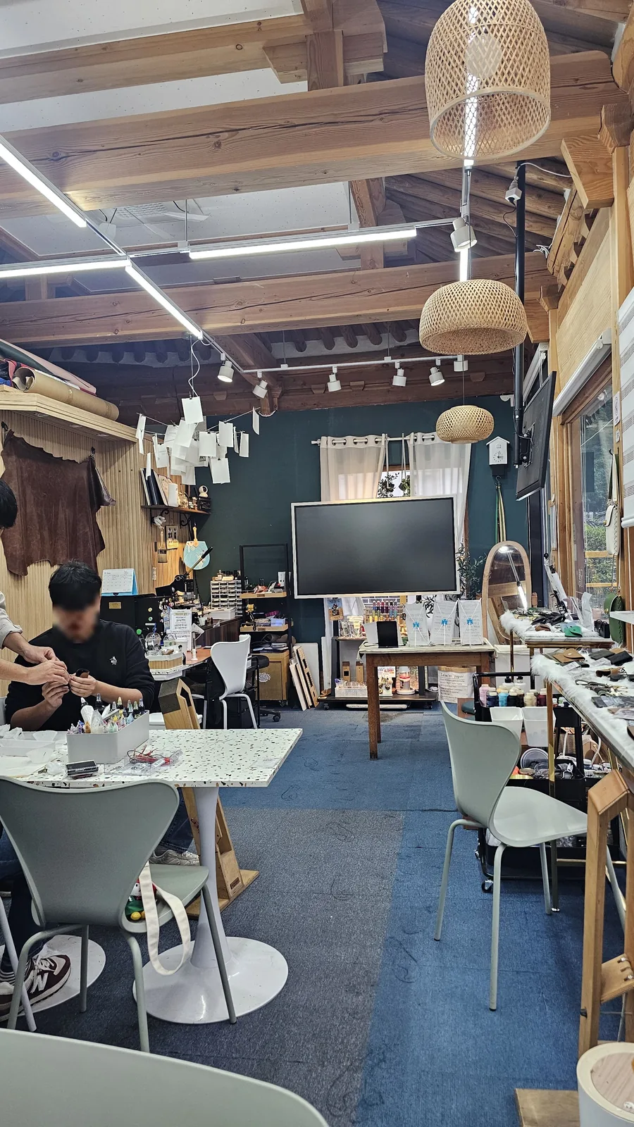 Interior of Amado Leather Workshop with traditional hanok wooden ceiling, craftsman working at a worktable in the background