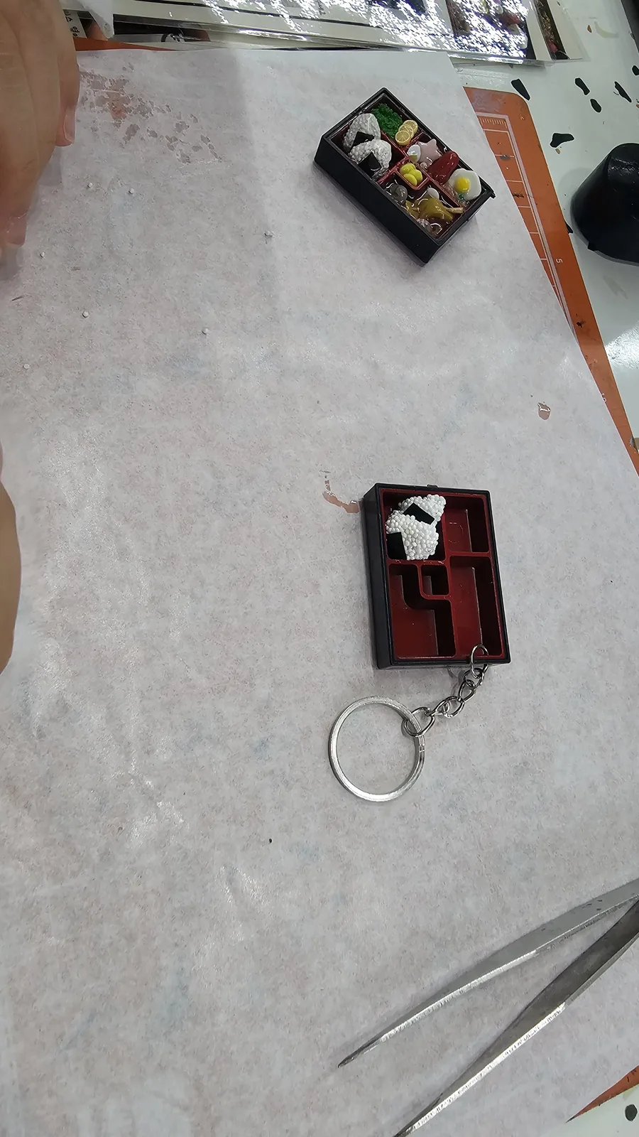 Mid-progress lunchbox keyring with one clay rice ball placed inside the acrylic frame