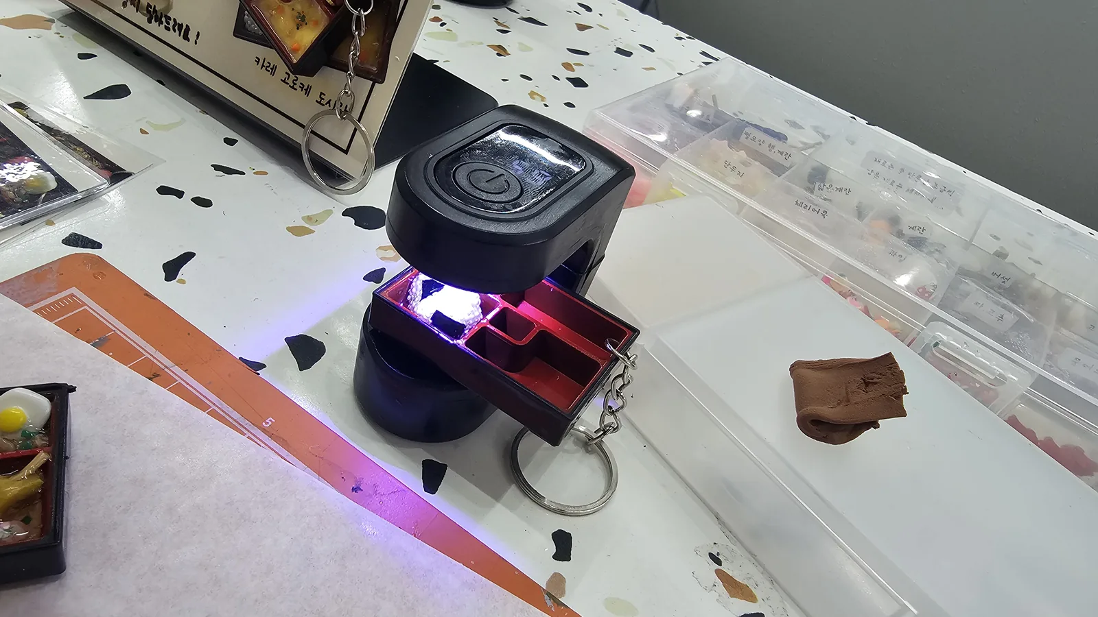 UV lamp curing the lunchbox keyring resin at Amado Leather Workshop, ingredient jars visible in background