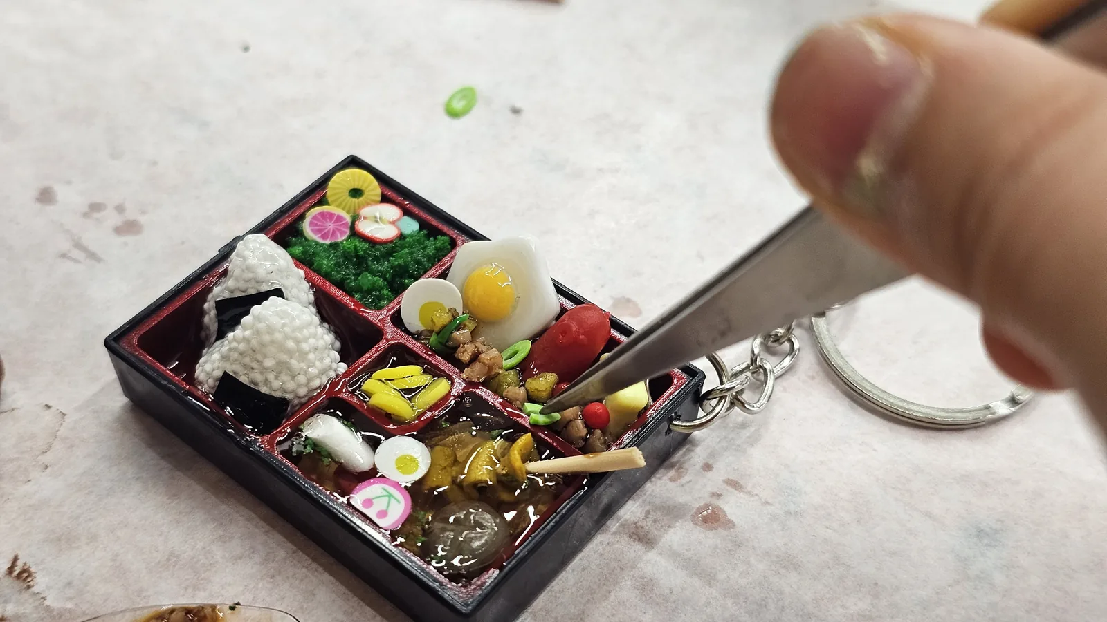 Hand holding an almost-finished lunchbox keyring while making final adjustments with tweezers