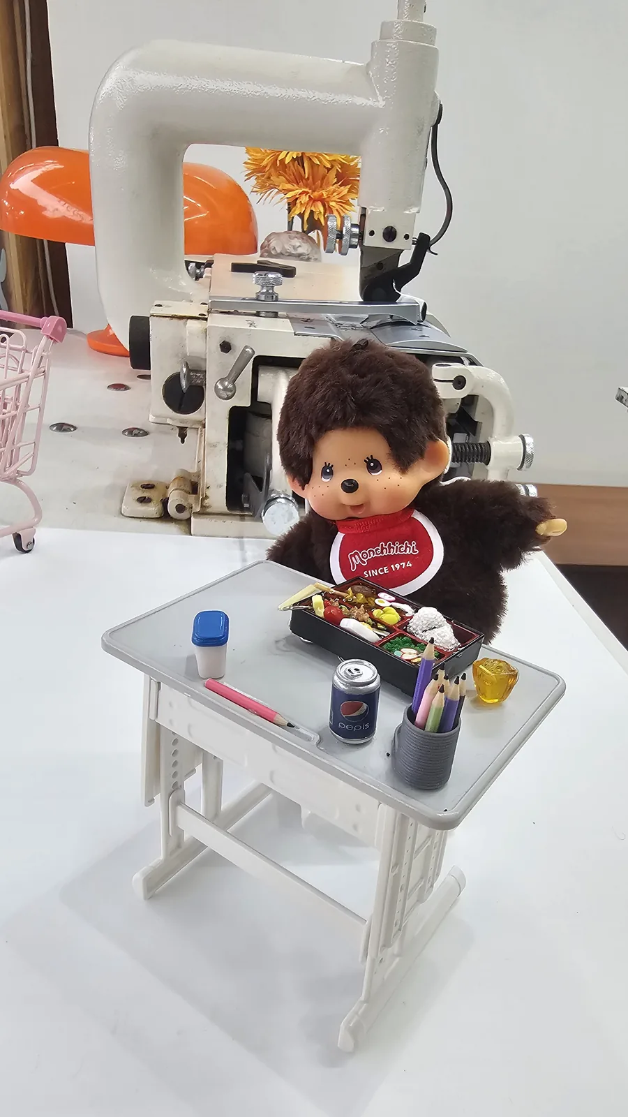 Finished lunchbox keyring displayed on a miniature school desk beside a Monkichi plush doll at Amado