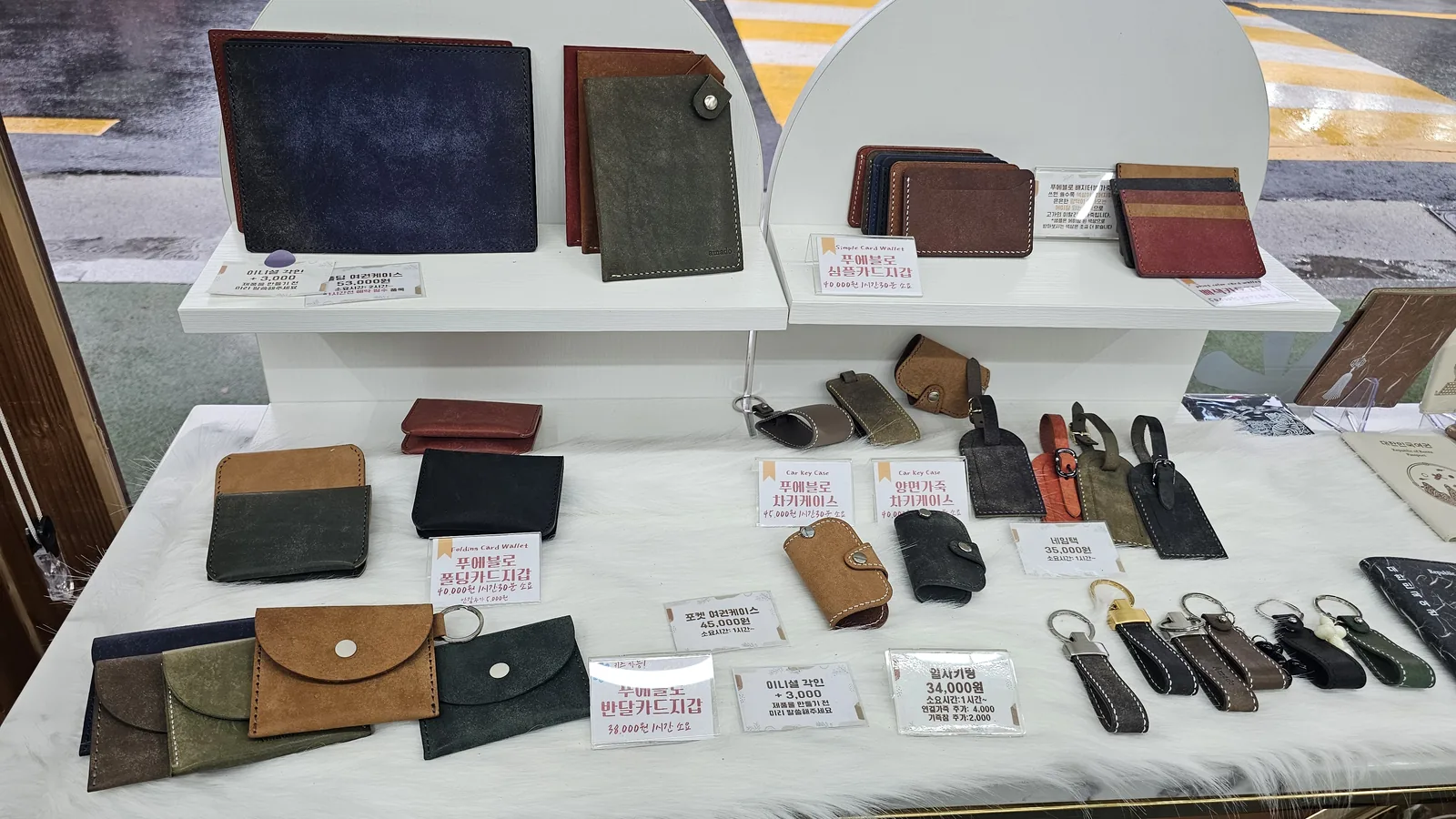 One-day class leather products displayed with price tags at Amado, including card wallets, car key cases, AirPods cases