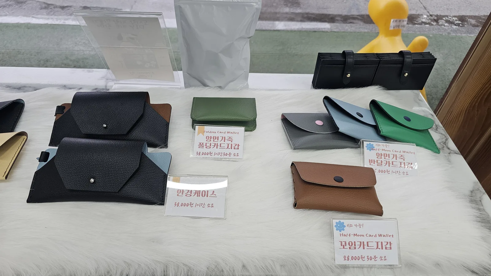 Leather product display at Amado showing double-sided folding card wallet, glasses case, and twisted card wallet