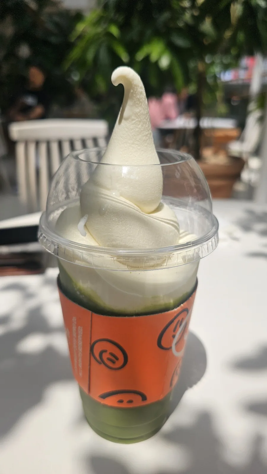 BERG Matcha Eibsee soft ice cream drink with orange cup sleeve on outdoor table in summer sunlight