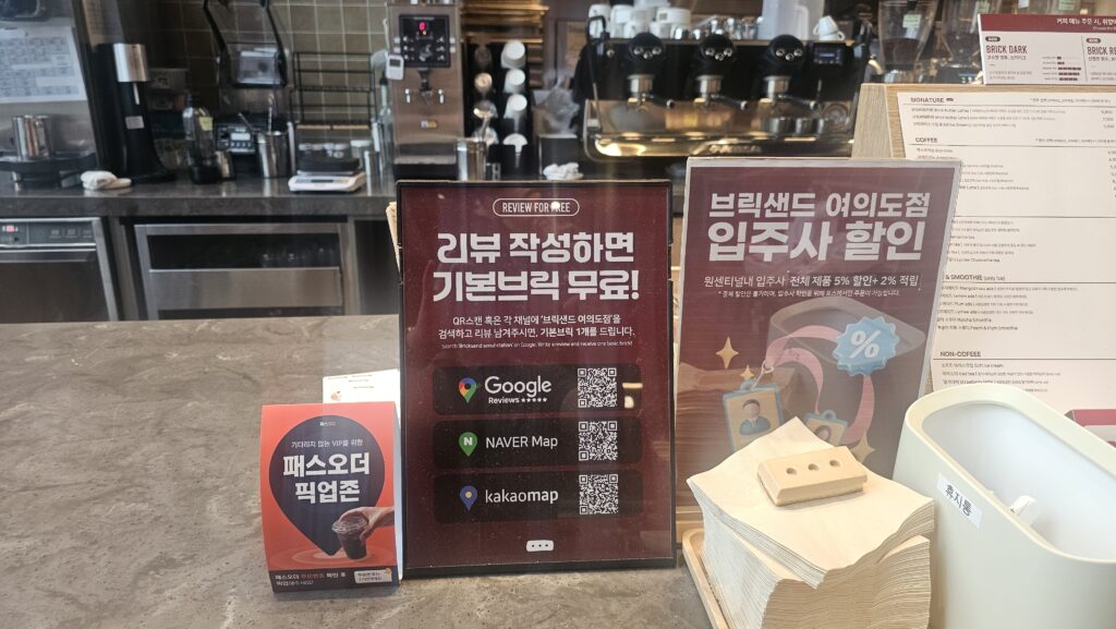 Counter notice board at Bricksand Coffee Yeouido showing review event promotion, building tenant discount, and Pass Order pickup zone signs
