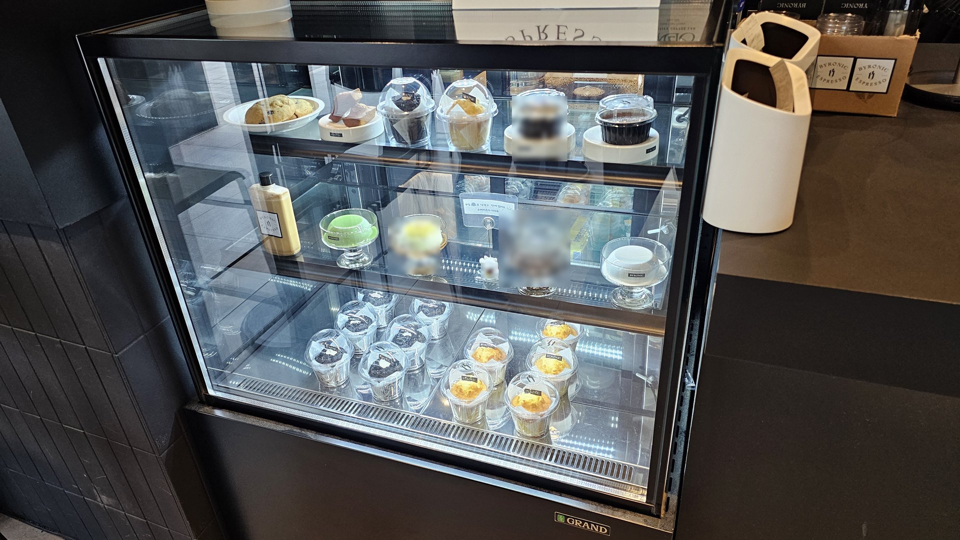 Three-tier glass pastry showcase at Byronic Espresso Yeouido displaying cupcakes, muffins, macarons, and egg tarts