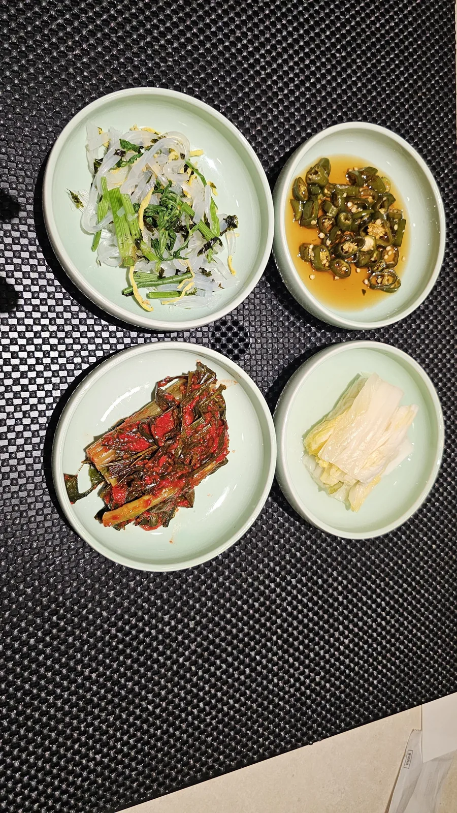 Four banchan side dishes at Daedong Jangeo — bean sprout, pickled green chili, green onion kimchi, and white kimchi