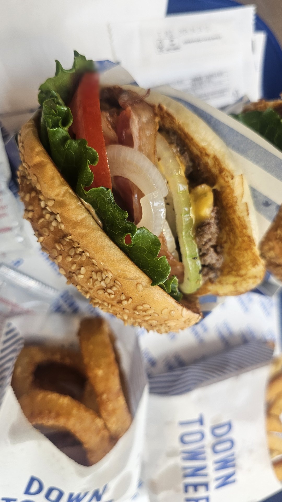 Downtowner Burger cross-section showing tomato, lettuce, onion, pickle, smash patty, and sesame bun