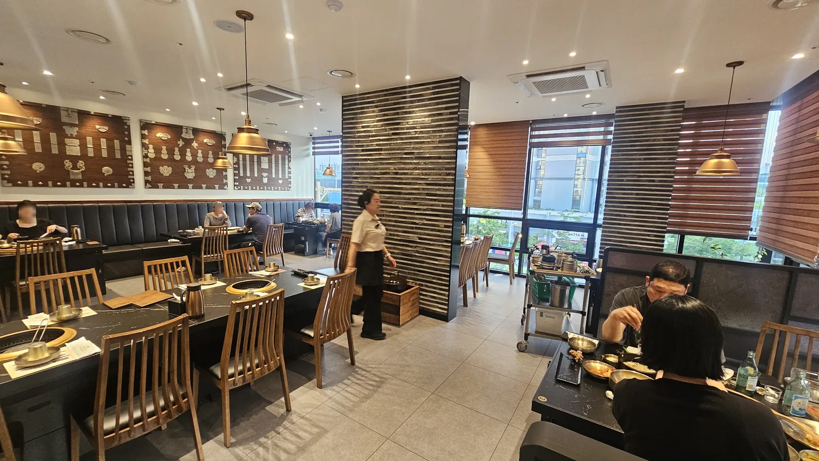 Elegant interior of Galbidorak Guro with wooden panels, brass pendant lights, and charcoal grill tables