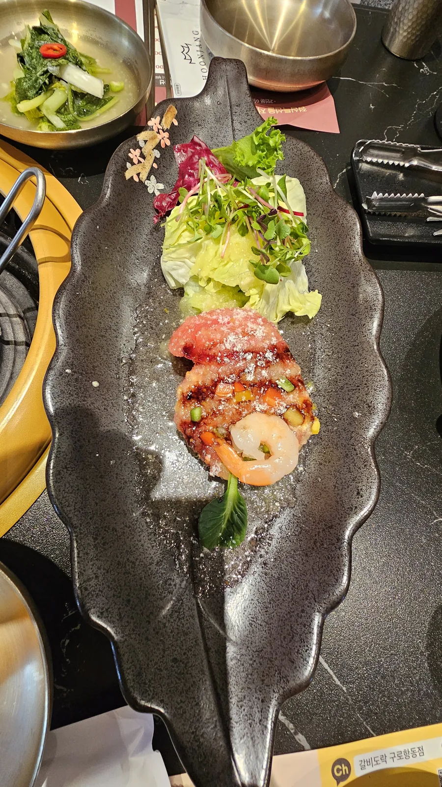 Galbidorak signature appetizer — beef yukhoe and shrimp on black leaf-shaped plate with micro greens and edible flowers