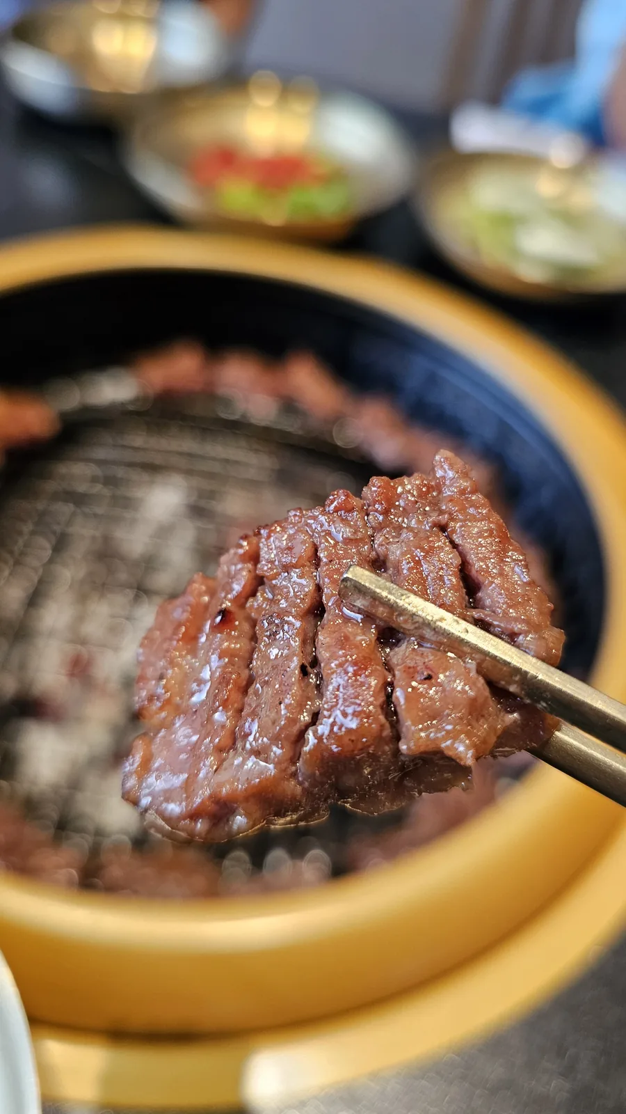 Brass tongs lifting a piece of well-cooked marinated beef at Galbidorak charcoal BBQ