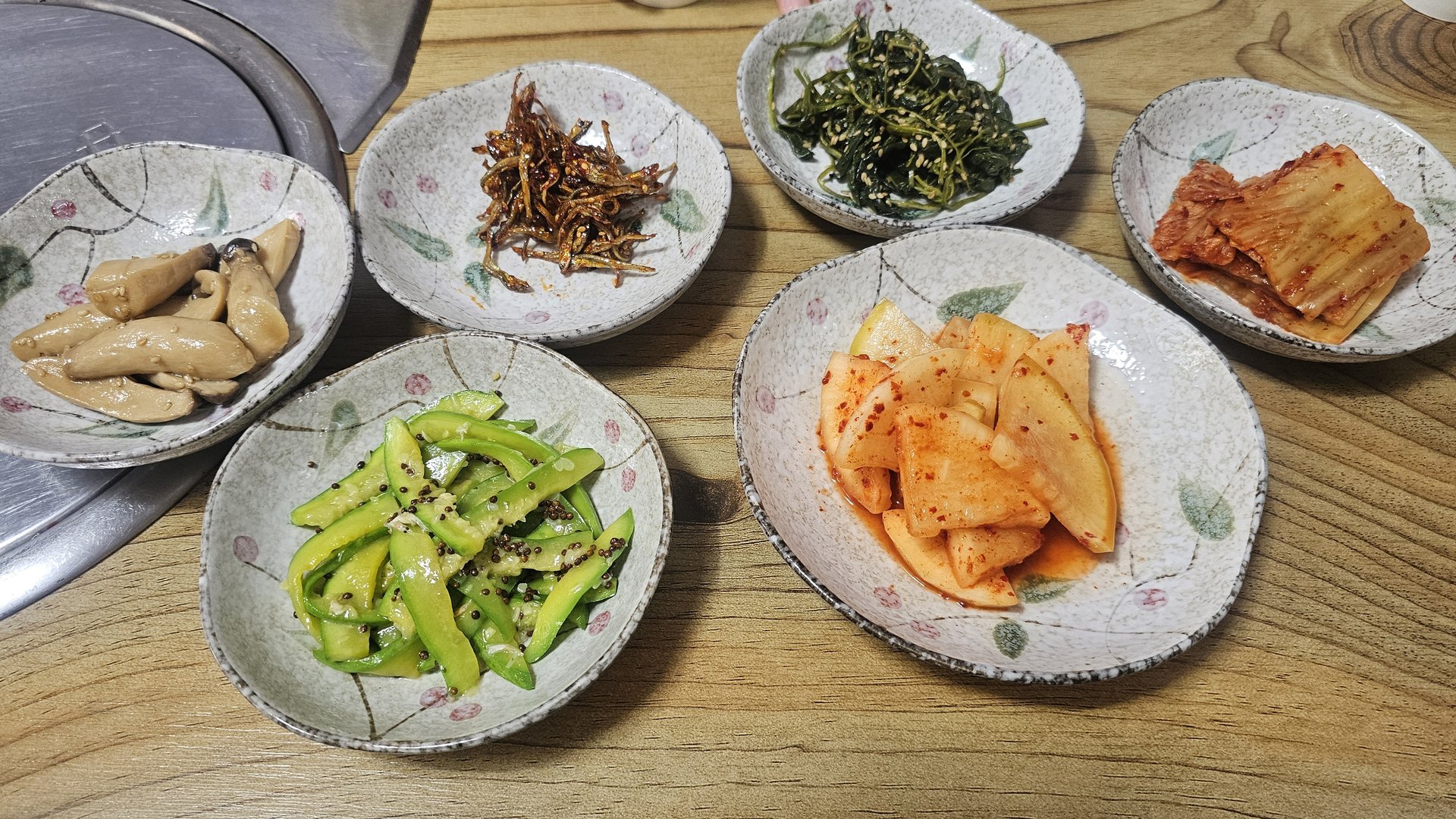 Five Korean banchan side dishes at Gareung Sikdang including pickled ginger, stir-fried anchovies, chwinamul greens, kkakdugi radish kimchi, and cucumber salad