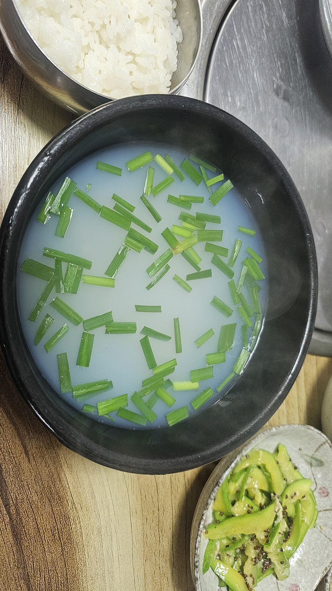 Bowl of jaecheop jinguk freshwater clam soup with chopped green onions and a side of steamed rice at Gareung Sikdang Hadong