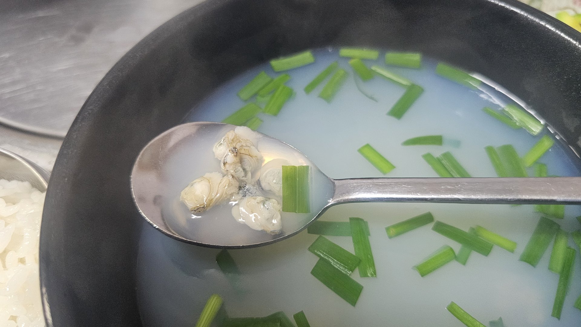 Close-up spoonful of jaecheop jinguk showing plump Seomjin River freshwater clams from Gareung Sikdang