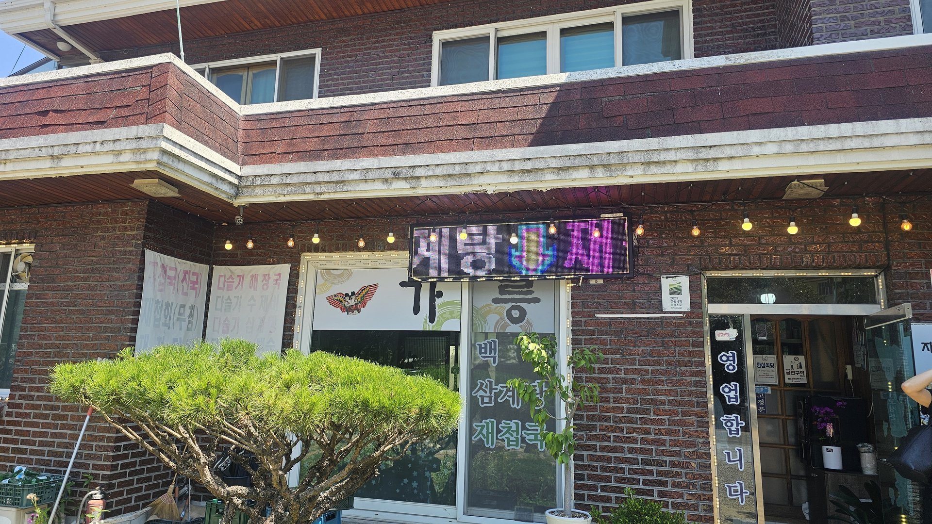 Exterior front of Gareung Sikdang in Hadong — red brick building with neon sign and handwritten menu on glass door