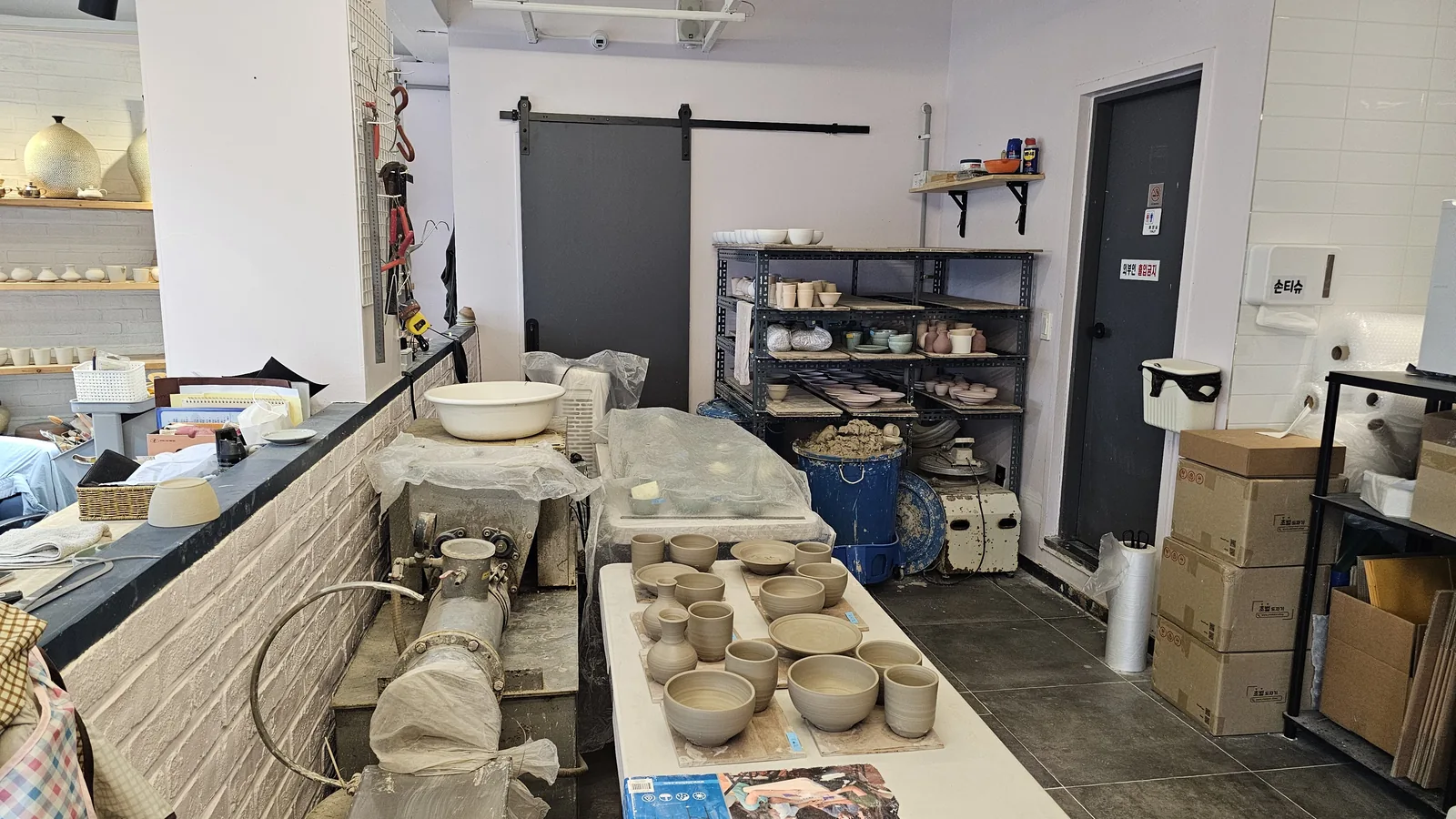 Interior of Udoye Gongbang pottery studio with pottery wheels, drying clay pieces, and shelving racks
