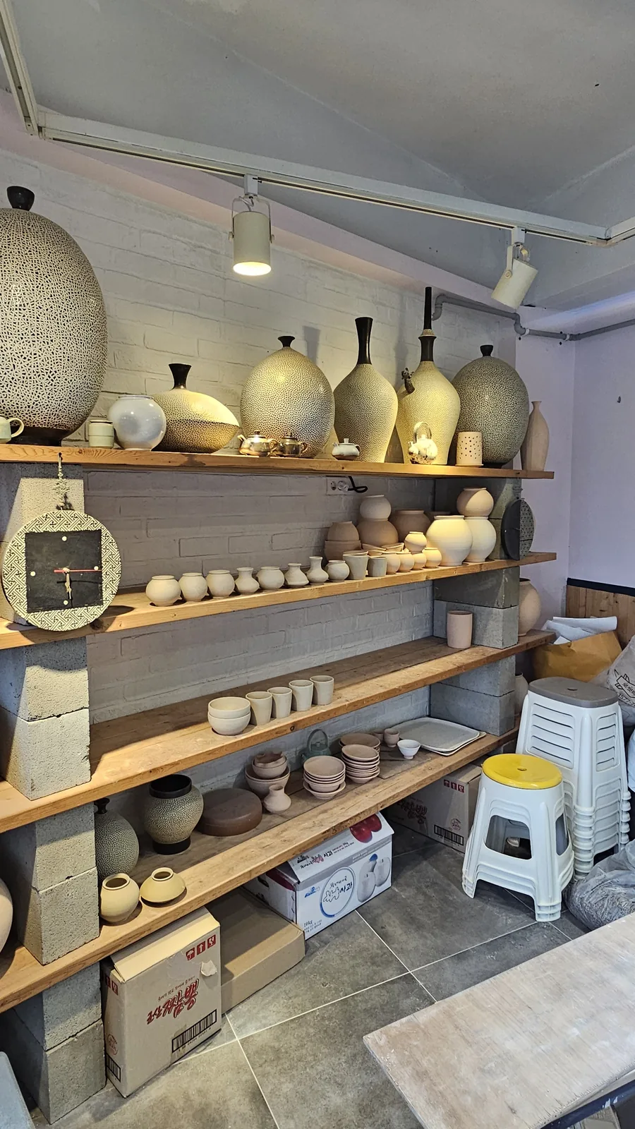 Full wall display shelves packed with ceramic works including jars, cups, bowls, and clock at Udoye Gongbang