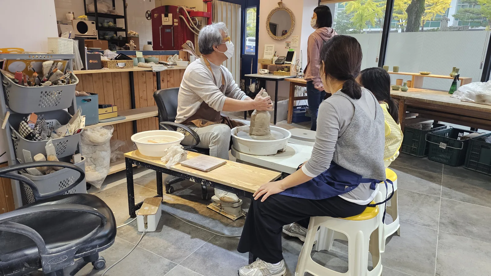 Pottery instructor demonstrating wheel technique while female participant observes at Udoye Gongbang