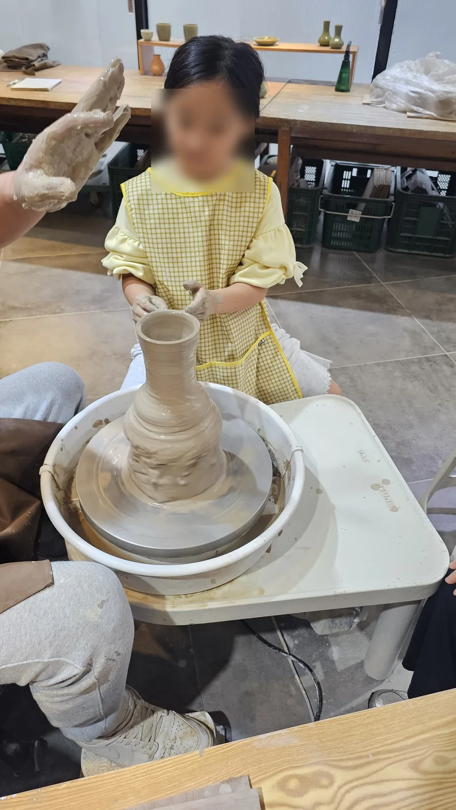 Young girl concentrating on forming a vase shape on the pottery wheel at Udoye Gongbang Jeonju