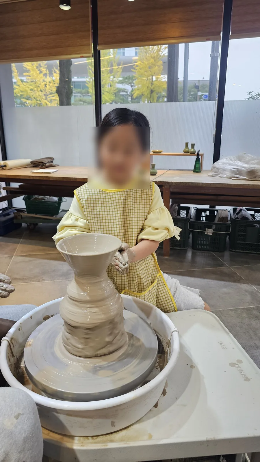 Young girl focused on holding the vase form alone on the pottery wheel at Udoye Gongbang
