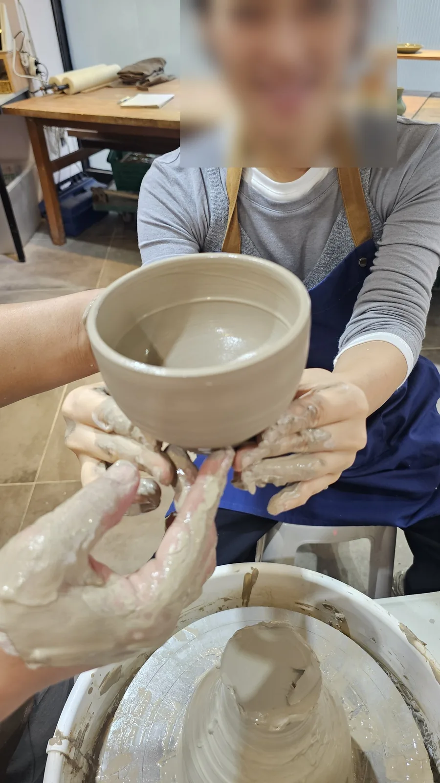 Adult woman with clay-covered hands holding her finished ceramic cup and smiling at Udoye Gongbang