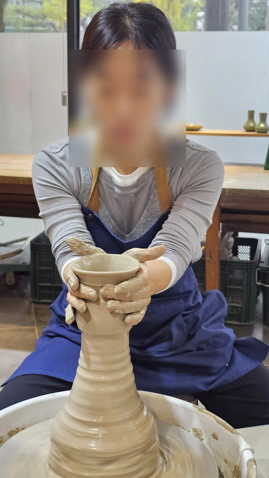 Adult woman concentrating on shaping a vase form on the pottery wheel at Udoye Gongbang Jeonju