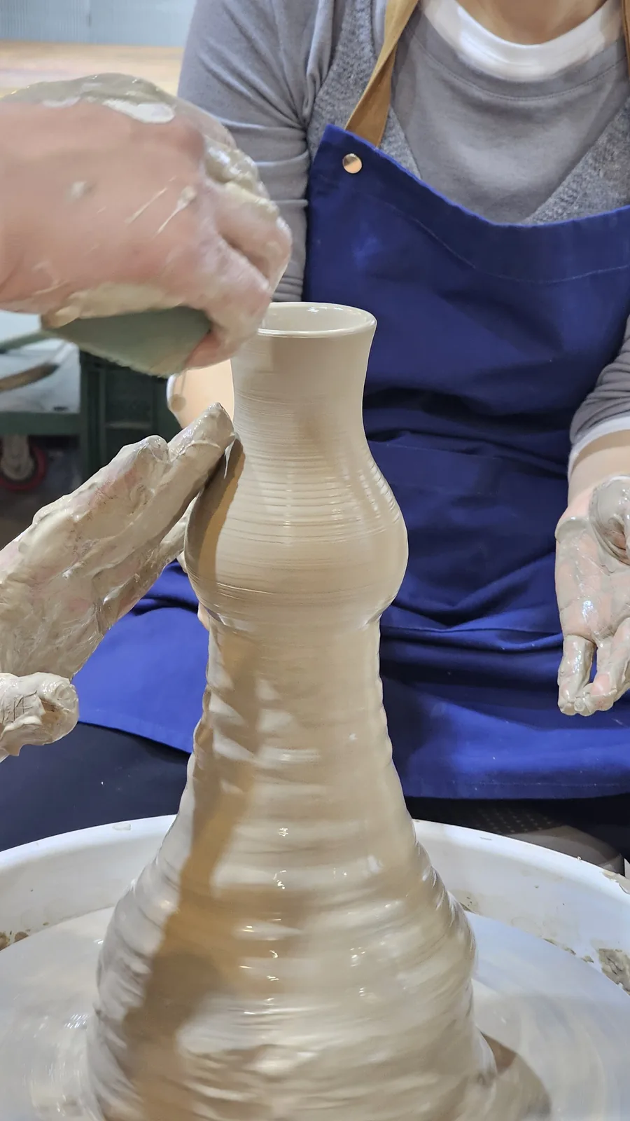 Close-up of hands forming a vase on the pottery wheel with instructor guidance at Udoye Gongbang