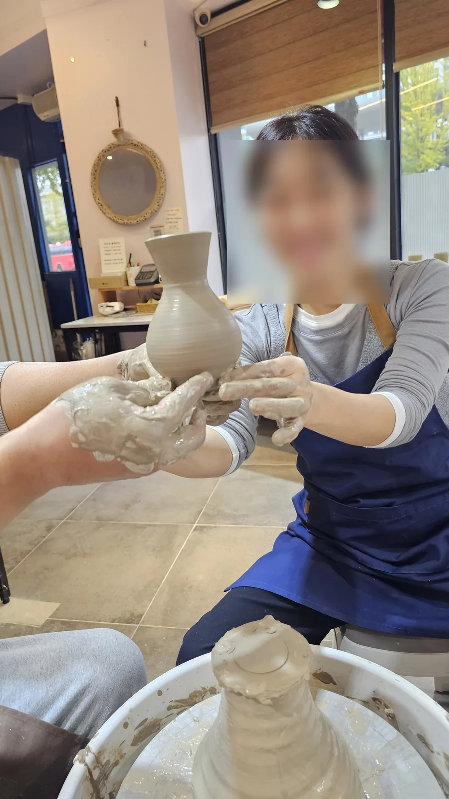 Adult woman holding her completed ceramic vase with both hands and looking at camera at Udoye Gongbang