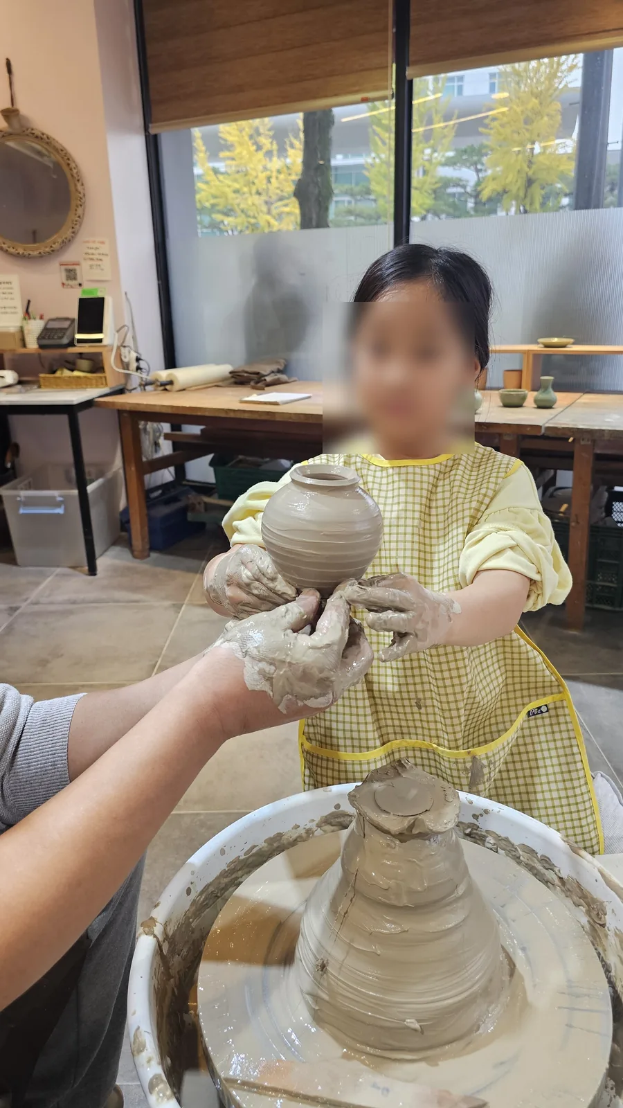 Young girl holding finished ceramic jar and looking directly at camera at Udoye Gongbang pottery studio