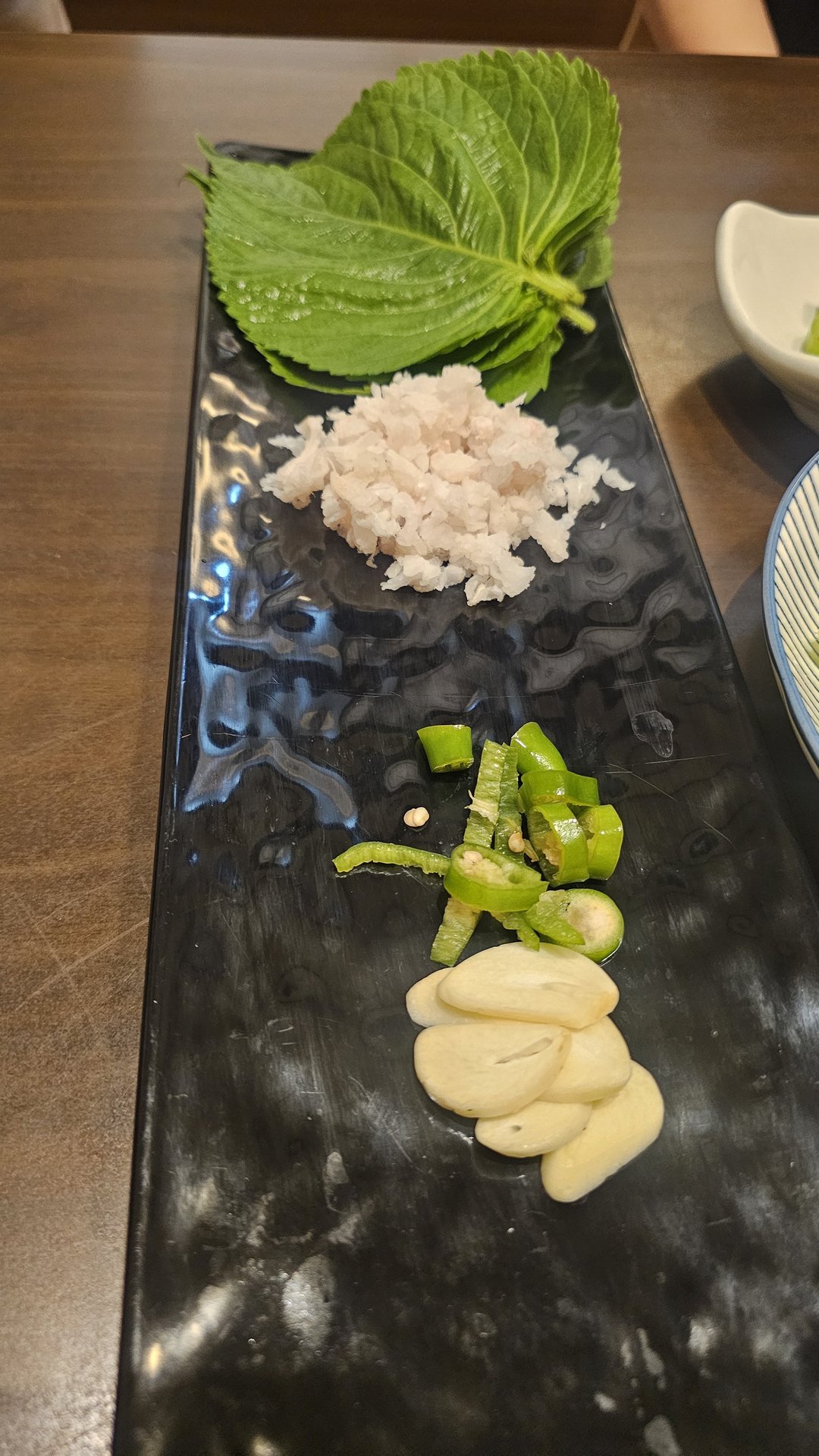 Ssam wrapping ingredients tray with perilla leaves, salted greens, green chili, and whole garlic at Ginza Yeouido