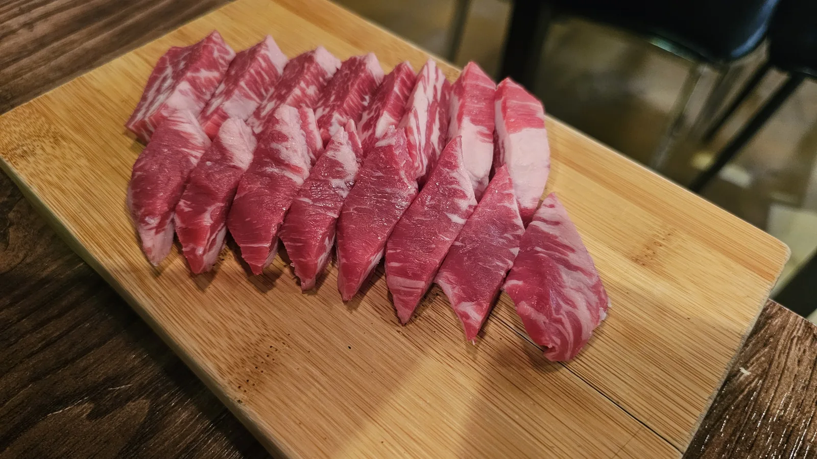Richly marbled raw beef on bamboo cutting board at GU.I Yeouido, close-up