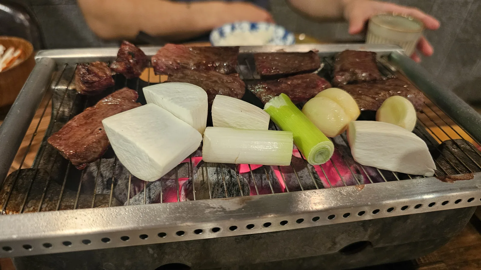 Beef slices and vegetables including radish and green onion grilling together on charcoal at GU.I Yeouido