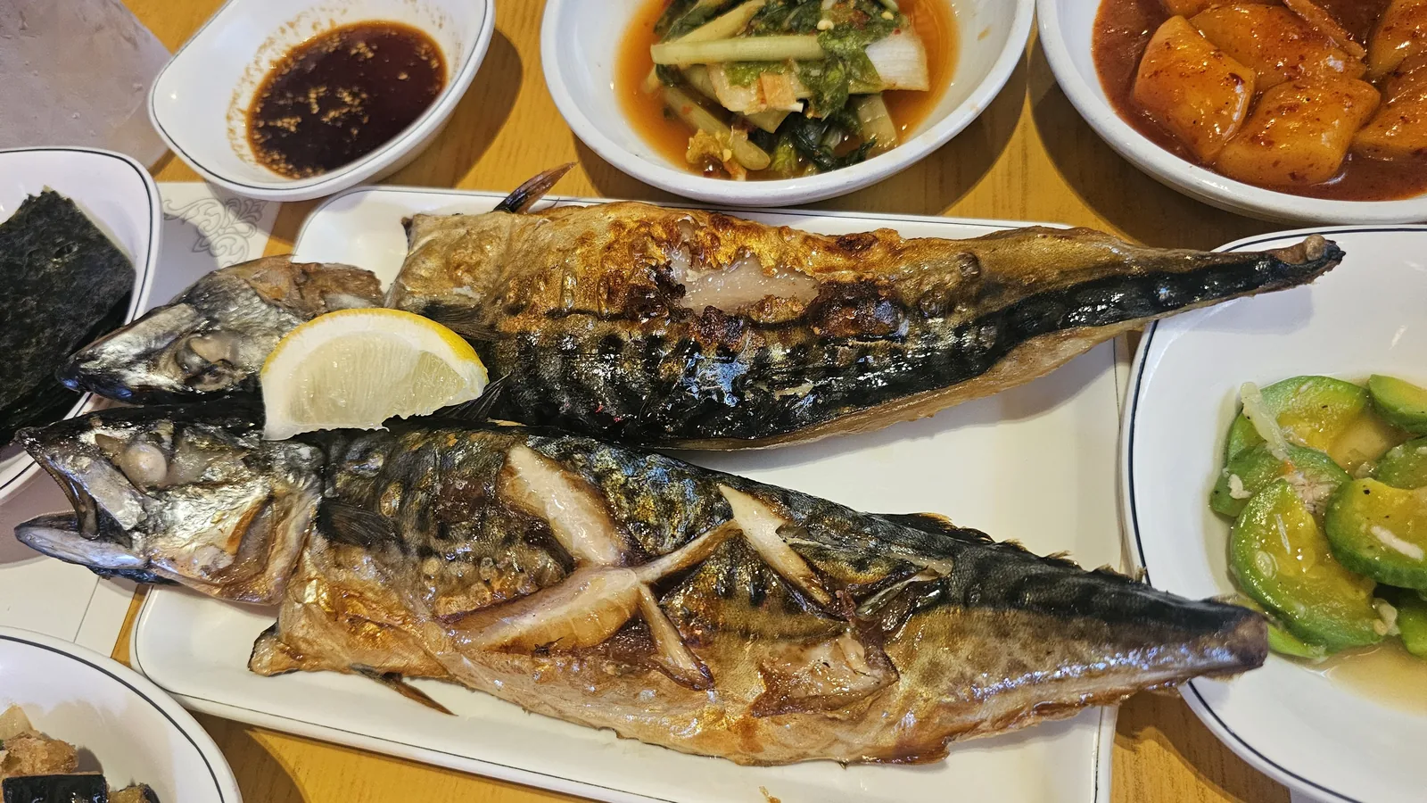 Two whole grilled mackerel with lemon slices at Guigui Yeouido, crispy golden skin close-up