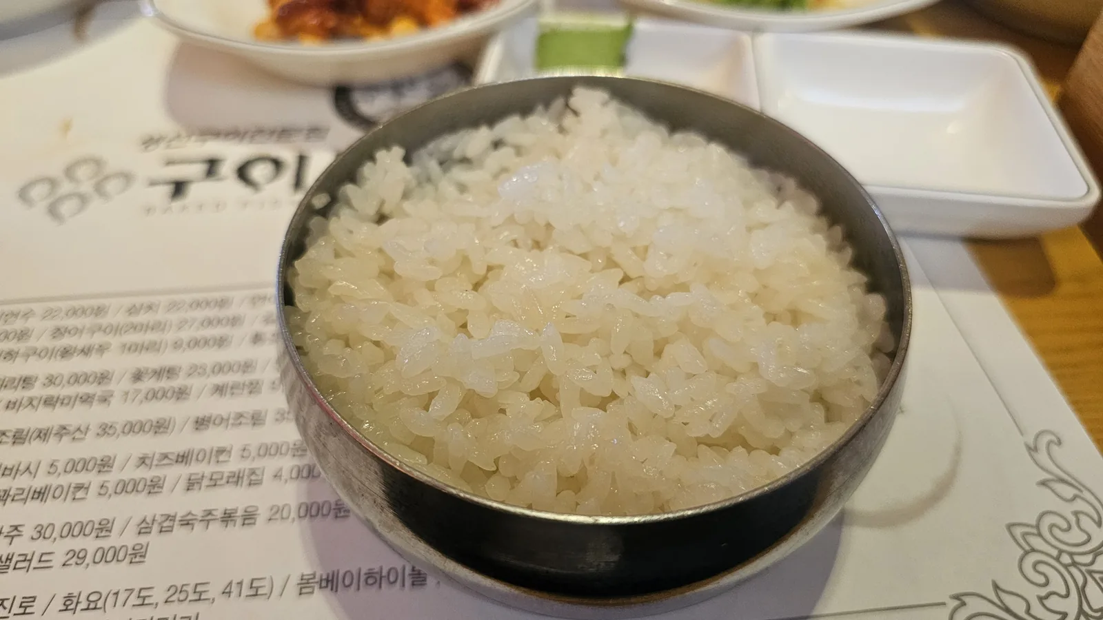 Steel bowl of white rice at Guigui Yeouido with menu board visible in the background