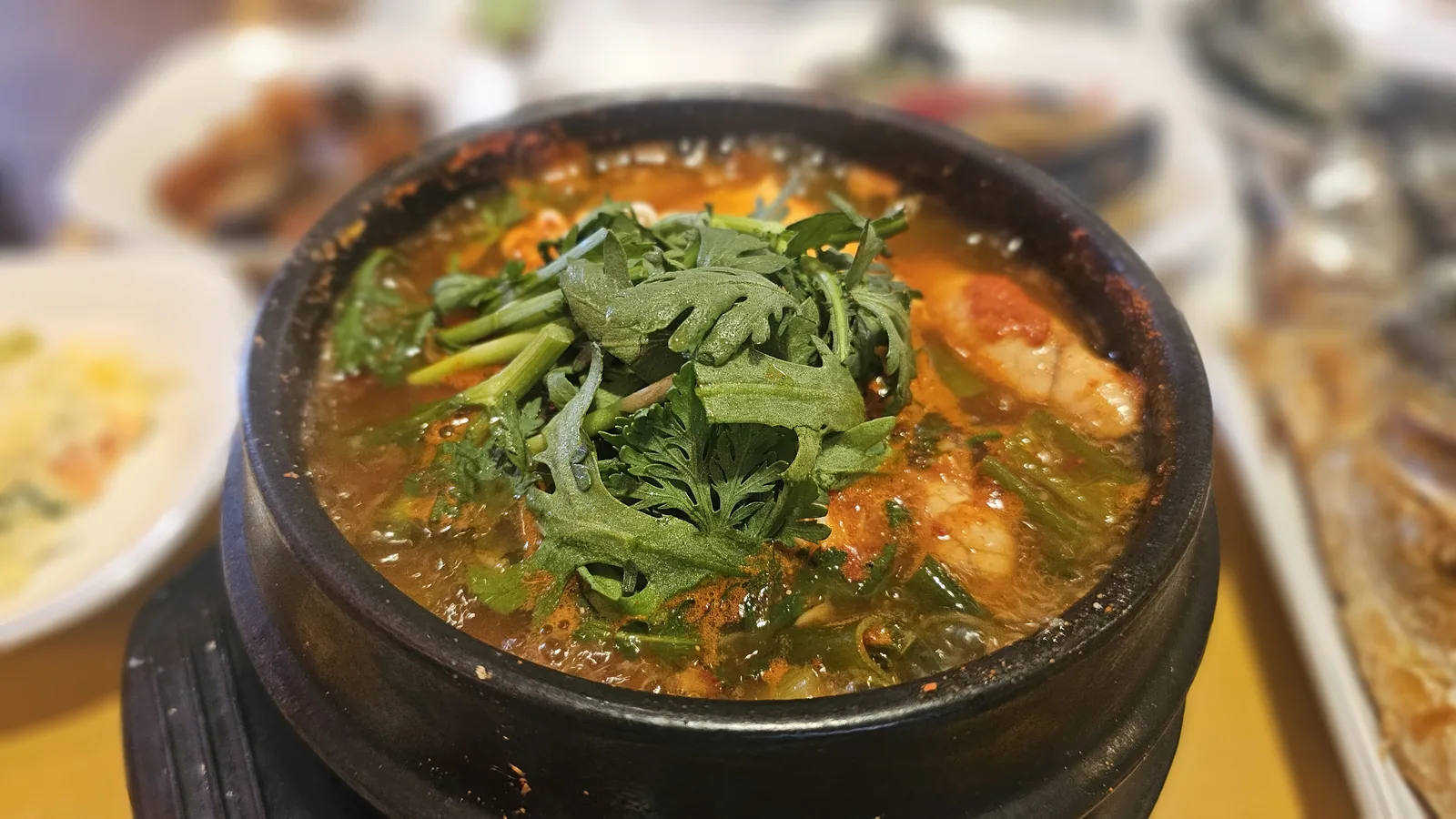 Spicy fish stew in earthenware pot at Guigui Yeouido garnished with green onions and water parsley