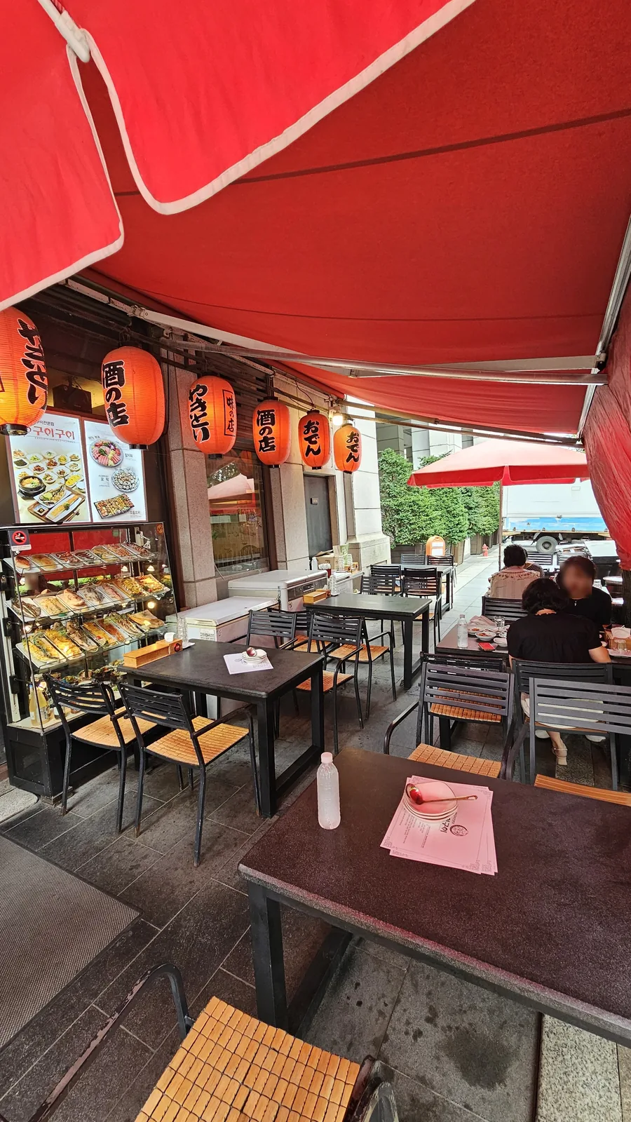Outdoor terrace seating at Guigui Yeouido with red awnings and orange paper lanterns