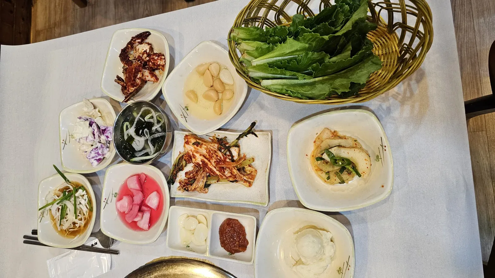 Full banchan spread at Haeoeum including ssam vegetables, whole garlic, pa-kimchi, pickled radish, tofu, cucumber salad, and cabbage salad
