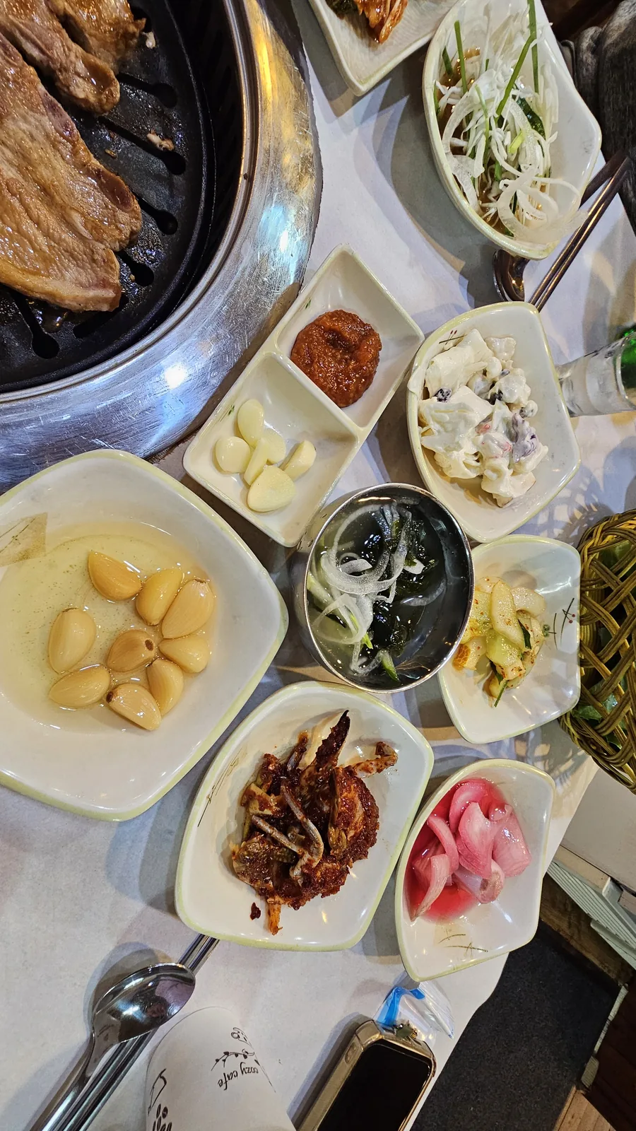 Pork ribs grilling on tabletop grill with whole garlic, pickled onion, and anchovy banchan dishes around it