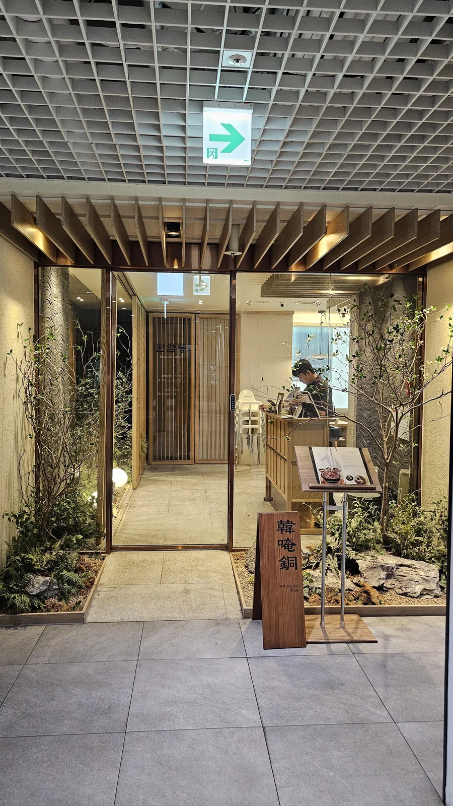 Hanam-dong restaurant entrance corridor with wood paneling, rough stone walls, and live plants in traditional Korean style