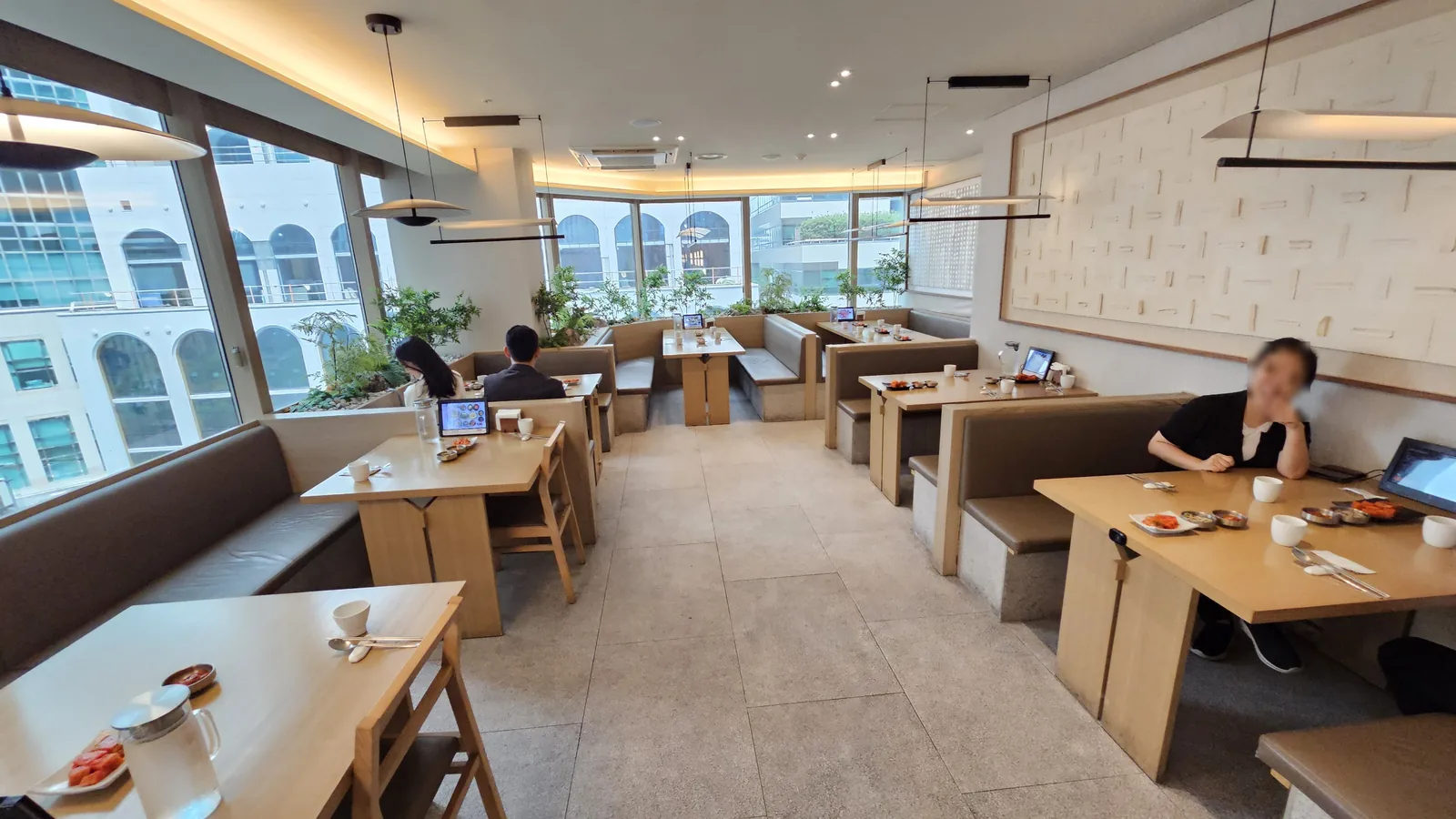 Hanam-dong interior dining hall with booth-style fabric sofa seating, tablet order kiosk, and large windows overlooking Yeouido office buildings