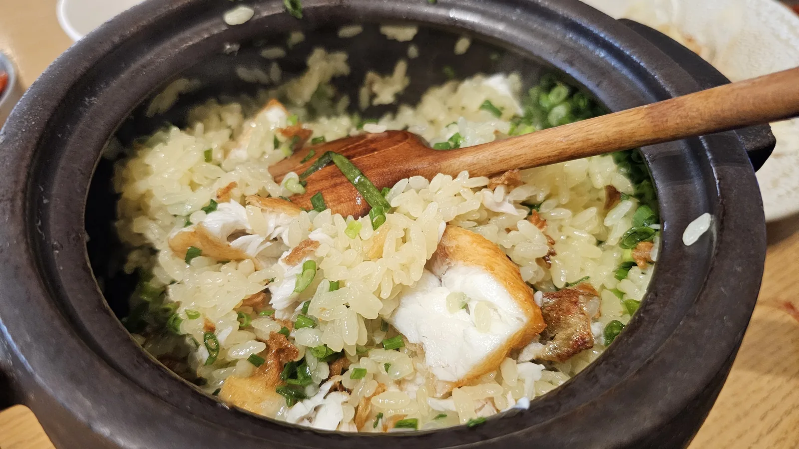 Mixing sea bream stone pot rice with wooden spatula at Hanam-dong, combining grilled fish flakes, scallion, and charred bottom rice