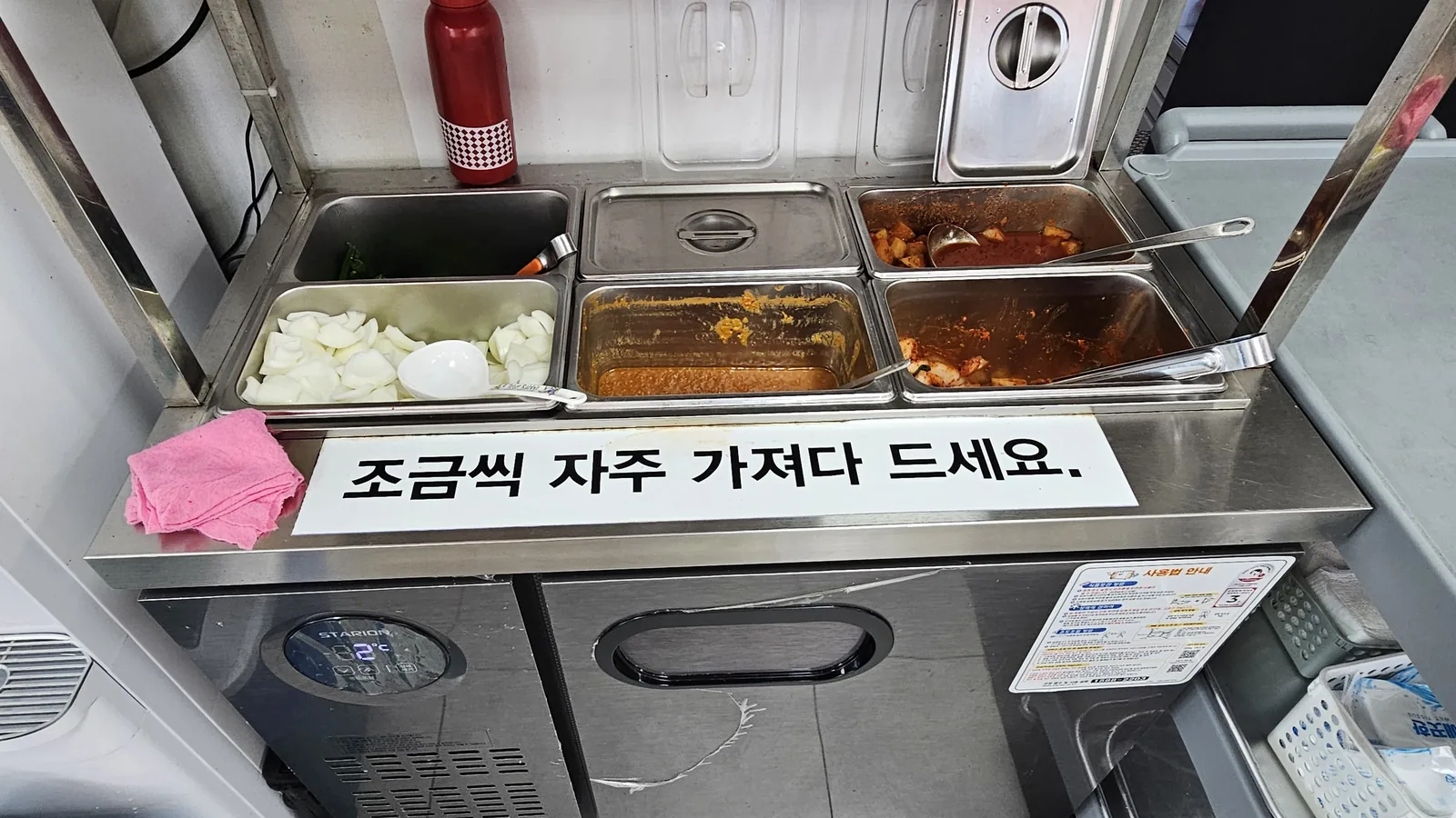 Self-service side dish bar at Hwanggeum Dwaeji Gukbap with stainless containers of onions, salted shrimp and kkakdugi