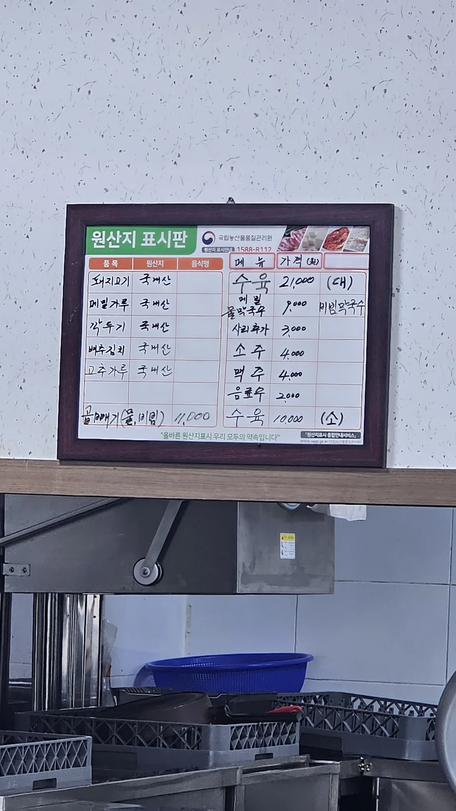 Wall-mounted ingredient origin sign at Jangsu Makguksu showing buckwheat and pork sourcing information in Korean