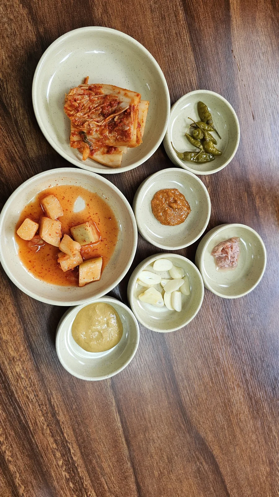 Seven-dish banchan spread at Jangsu Makguksu including kkakdugi radish kimchi, baechu kimchi, doenjang, and mustard sauce