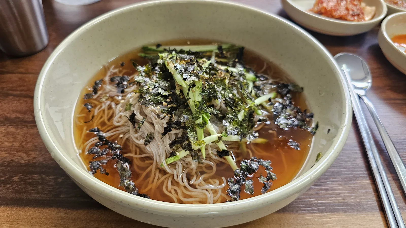 Bowl of buckwheat makguksu with clear cold broth, shredded cucumber, and dried seaweed flakes at Jangsu Makguksu