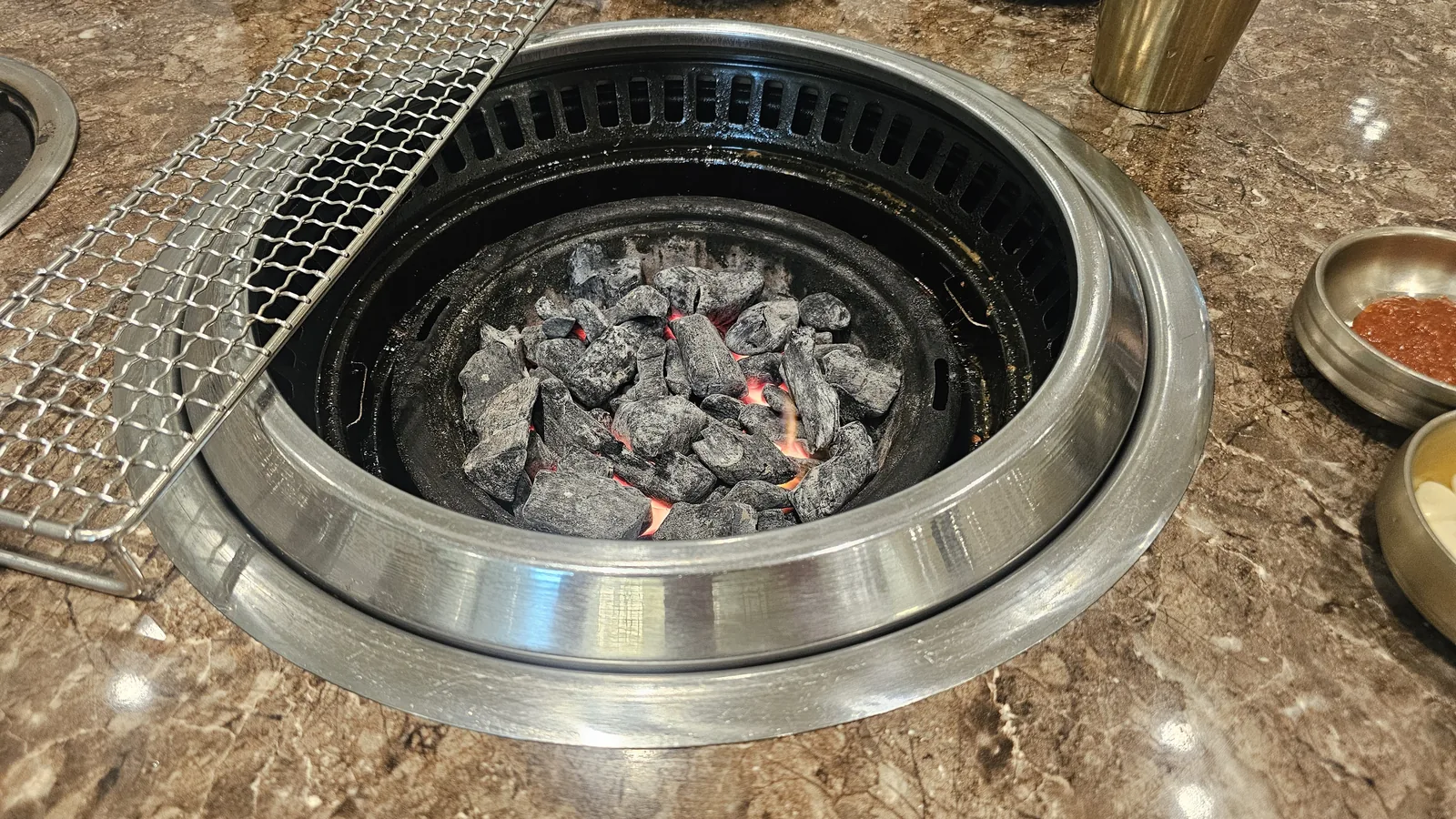 Round charcoal brazier setup with grill grate and condiments before lighting at Jogane Galbi Mokdong
