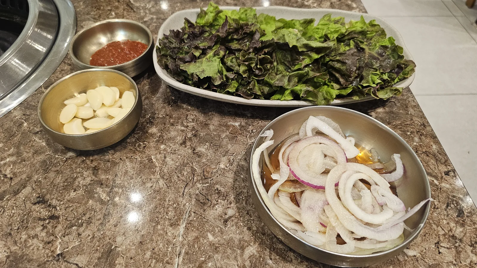 Korean BBQ side dish spread at Jogane Galbi — perilla leaves, lettuce, garlic, pickled onion, and ssamjang paste