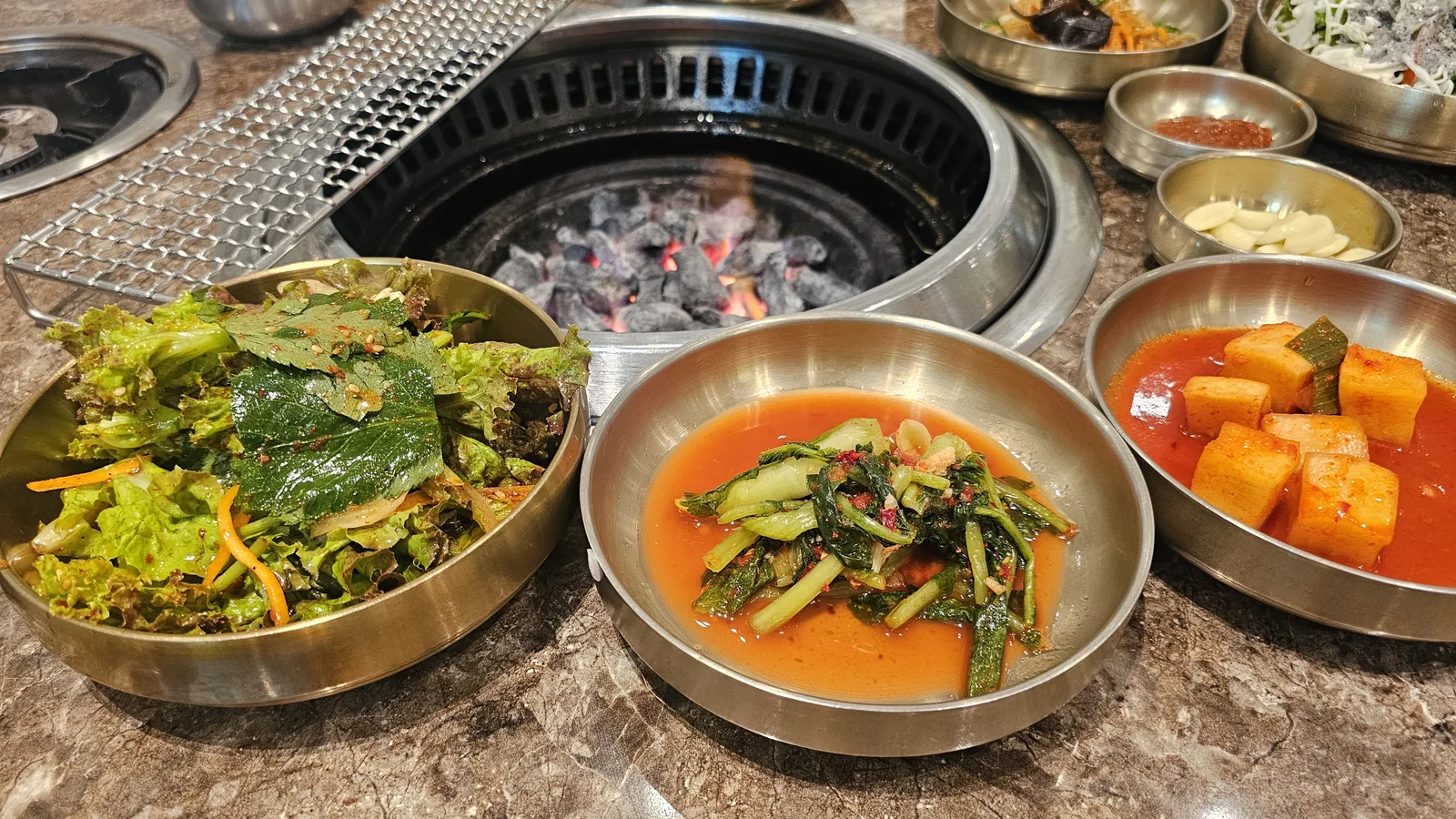 Full table setup at Jogane Galbi Mokdong after charcoal lighting — ssam vegetables, kimchi, and grill ready
