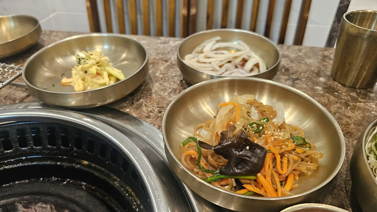 Korean BBQ side dishes at Jogane Galbi — japchae glass noodles, macaroni salad, and pickled onion slices