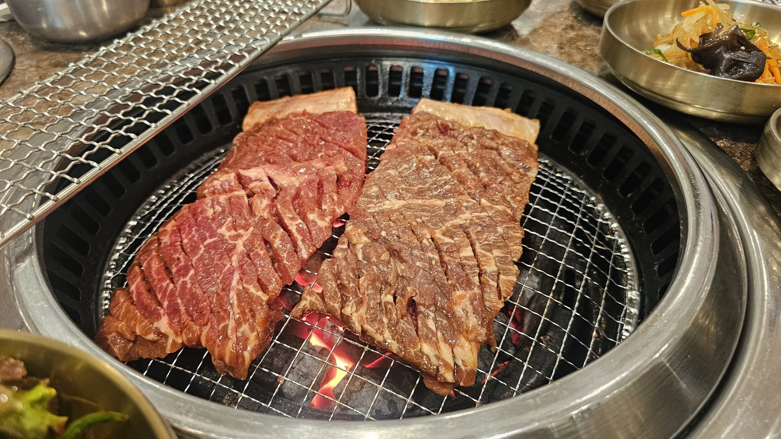 Raw and marinated beef short ribs in early stages of grilling over charcoal at Jogane Galbi